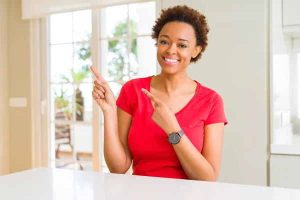 年轻美丽的非洲裔美国女人在家里微笑着 看着相机指向用两只手和手指的一侧 — 图库照片