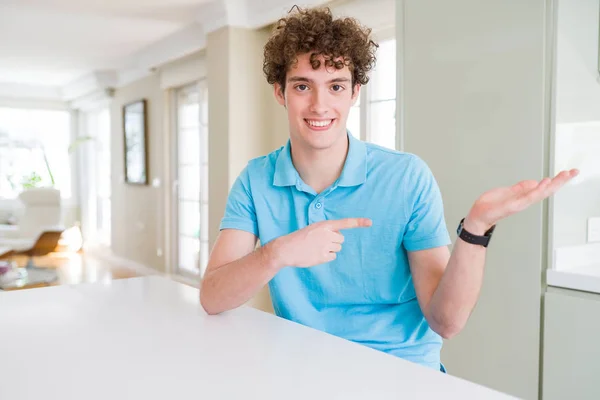 若いハンサムな男着てカジュアルなブルー シャツを家で驚くし 手とを提示 指で指している間カメラに笑顔 — ストック写真