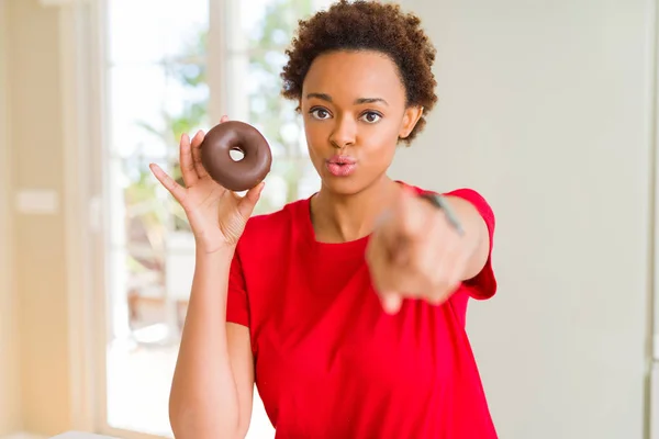 年轻的非洲裔美国妇女吃巧克力甜甜圈用手指指着相机和你 手的标志 积极和自信的手势从前面 — 图库照片