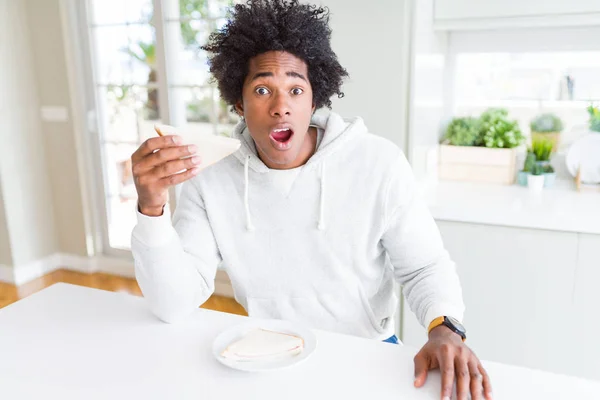 African American man eating handmade sandwich at home scared in shock with a surprise face, afraid and excited with fear expression