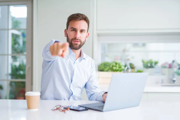 Handsome man working using computer laptop and drinking a cup of coffee pointing with finger to the camera and to you, hand sign, positive and confident gesture from the front