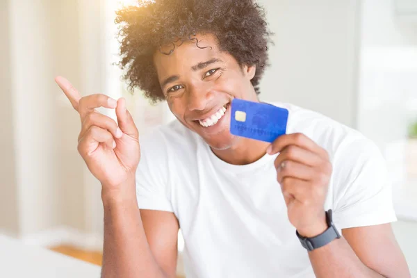 African American man holding credit card very happy pointing with hand and finger to the side