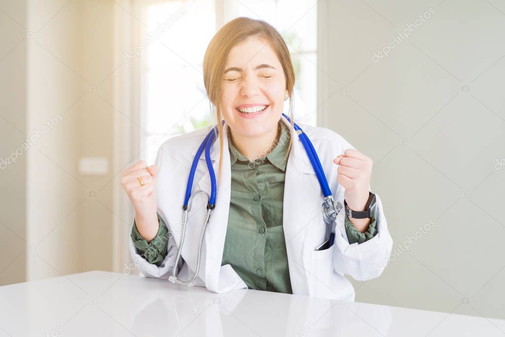 Beautiful young doctor woman wearing medical coat and stethoscope very happy and excited doing winner gesture with arms raised, smiling and screaming for success. Celebration concept.