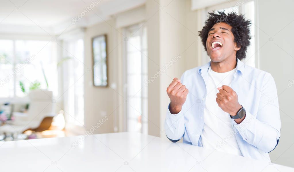 African American man at home very happy and excited doing winner gesture with arms raised, smiling and screaming for success. Celebration concept.
