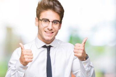 El ile pozitif jest yapıyor izole arka plan başarı işareti üzerinde gözlük takan genç iş adamı başparmak gülümseyen ve mutlu. Neşeli bir ifadeyle, kazanan jest kameraya bakıyor.