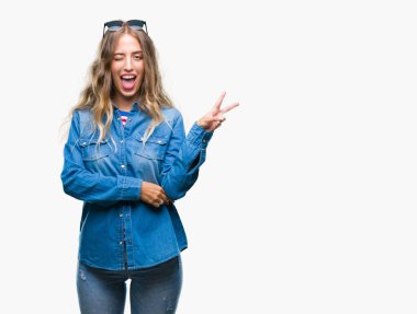 Mutlu yüz zafer işareti yaparken kameraya göz kırpıyor ile gülümseyen izole arka plan üzerinde güneş gözlüğü takıyor güzel sarışın genç kadın. İki numaralı.