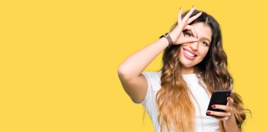 Mutlu yüz el parmaklarının arasından seyir göz üzerinde ok işaretiyle yapıyor gülümseyen ile akıllı telefon kullanan genç yetişkin kadın