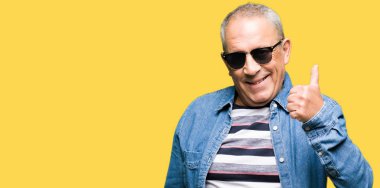 Denim ceket ve hareketi el ile mutlu yaşasın yaparken güneş gözlüğü takan yakışıklı komuta sizde. Kameraya bakarak başarı gösteren ile ifade onaylama.