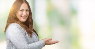 Artı boyutu genç kadın güzel kış ceket üzerinde izole arka plan el ve reklam mutlu ve kendinden emin gülümseyen sunulması avuç, yanında işaret