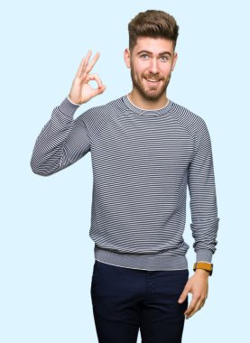 El ve parmak ile ok işareti yapıyor olumlu gülümseyen kazak giyen genç yakışıklı adam çizgili. Başarılı ifade.