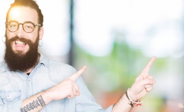 Uzun saç ve sakal gülümseyen ve iki elleri ve parmakları ile tarafına işaret kamera bakarak gözlüklü genç hipster adamla.