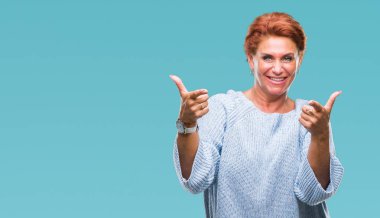 Fotoğraf makinesi ile mutlu ve komik yüz için parmakları işaret izole arka plan üzerinde kış kazak giyen Atrractive üst düzey beyaz Kızıl saçlı kadın. İyi enerji ve vibes.