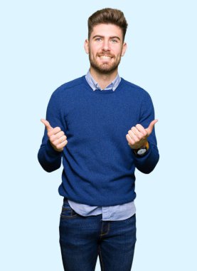 Genç yakışıklı bussines başarı işareti başparmak gülümseyen ve mutlu el ile pozitif jest yapıyor adamım. Neşeli bir ifadeyle, kazanan jest kameraya bakıyor.