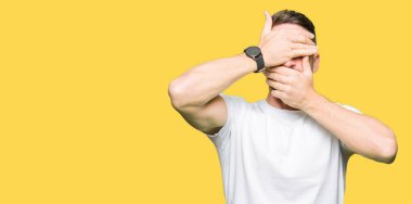 Yakışıklı adam giyiyor rahat beyaz t-shirt kapsayan gözleri ve şaşırttı ve şok ellerle ağız. Duygu gizleme