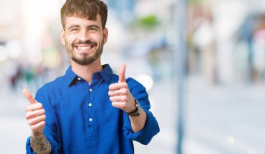 Yakışıklı delikanlı el ile pozitif jest yapıyor onaylama izole arka plan üzerinde başparmak gülümseyen ve başarı için mutlu. Kamera, kazanan jest arıyorsunuz.