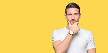 Yakışıklı adam emin çapraz kollar ve çeneme kaldırdı el ile gülümseme ile kameraya bakarak casual beyaz t-shirt giyiyor. Pozitif düşünce.