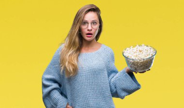 Genç güzel sarışın kadın izole arka şok sürpriz yüzü, korkuyor ve korku ifadesi ile heyecanlı olan korkmuş üzerinde patlamış mısır yemek