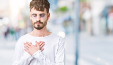 Yakışıklı delikanlı ile gülümseyen izole arka plan üzerinde güneş gözlüğü takıyor kapalı gözler ve yüzünde minnettar jest ile göğüs üzerinde eller. Sağlık kavramı.