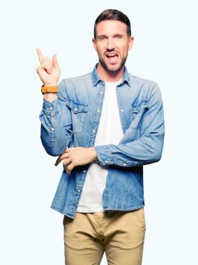 Yakışıklı adam kameraya bakarak yan el ve parmak ile işaret mavi gözleri ve denim ceket kocaman bir gülümseme ile yüzünde, sakal.