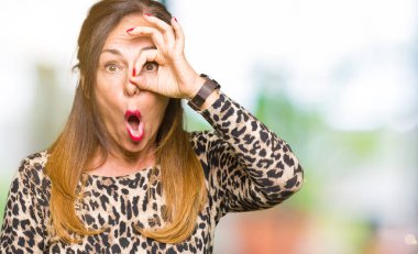 Sürpriz yüz, göz parmaklarının arasından seyir ile ok jest yapıyor leopar hayvan baskı elbise giyen güzel orta yaş kadın şok. İmansız ifade.