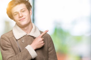 Genç yakışıklı adam giyen kış ceket izole üzerinden reklam, ciddi ve sakin yüz gösterilen yan el parmak ile işaret arka plan