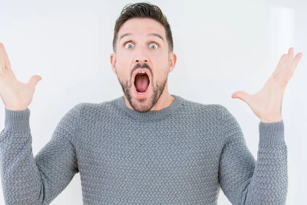 Üzerinde rahat kazak giyen genç yakışıklı adam deli kutluyor arka plan izole ve başarı için kaldırdı kollarını açarak hayrete ve heyecanlı çığlık gözleri açık. Kazanan kavramı