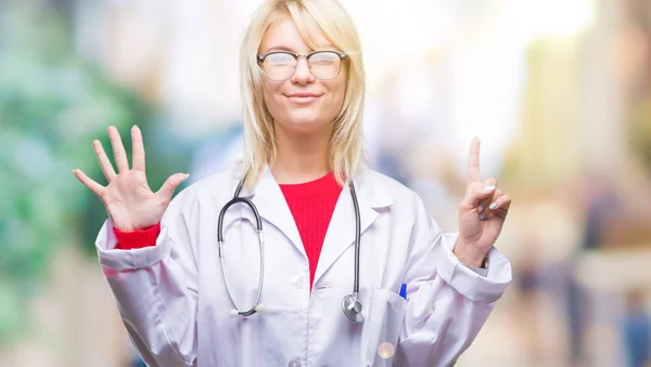 年轻美丽的金发医生妇女穿医疗制服在孤立的背景显示和指向与手指数字六同时微笑自信和快乐 — 图库照片