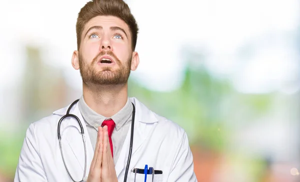 Νεαρός Γιατρός Όμορφος Άνδρας Φορώντας Ιατρική Παλτό Επαιτεία Και Προσεύχεται — Φωτογραφία Αρχείου