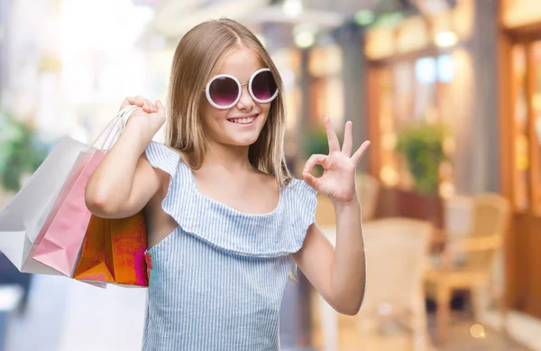 年轻美丽的女孩拿着购物袋在销售在孤立的背景做确定的标志与手指 优秀的象征 — 图库照片