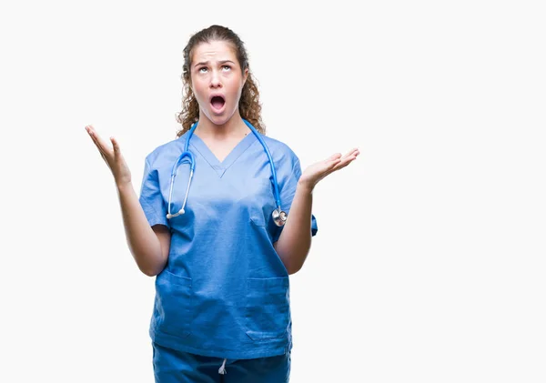 年轻的黑发医生女孩穿着护士或外科医生制服在孤立的背景疯狂和疯狂的喊声和大喊大叫与积极的表情和手臂抬起来 挫折的概念 — 图库照片