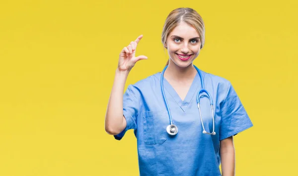 年轻美丽的金发医生护士妇女在孤立的背景微笑和自信的手势与手做大小标志与手指 而看和相机 测量概念 — 图库照片