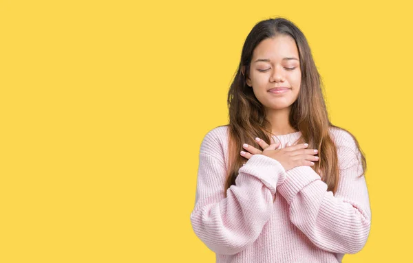笑みを浮かべて孤立の背景にピンク冬セーターを着ている若い美しいブルネットの女性は目を閉じてと感謝のジェスチャーの顔に胸に手します 健康の概念 — ストック写真