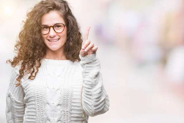 Gösterilen ve kendinden emin ve mutlu gülümseyen bir parmak ile işaret eden oktan yukarı izole arka plan üzerinde kış kazak giyen güzel esmer kıvırcık saçlı Genç kız.