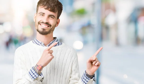 笑顔で側に つの手と指で指しているカメラを見て孤立の背景に冬のセーターを着ている若いハンサムな男 — ストック写真