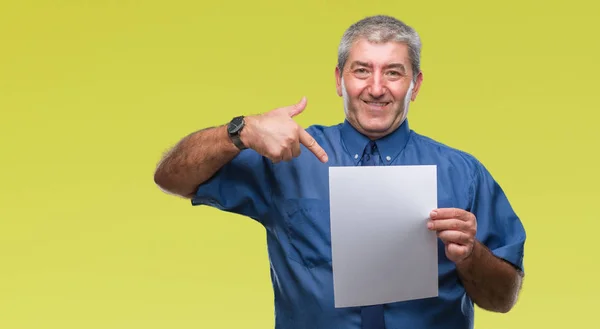 Handsome senior man holding blank sheet paper over isolated background with surprise face pointing finger to himself