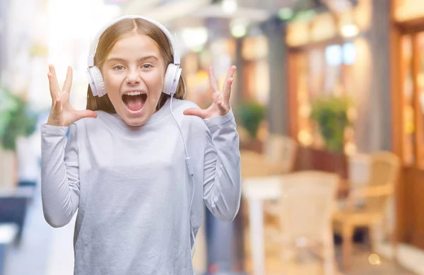 年轻美丽的女孩戴着耳机听音乐在孤立的背景庆祝疯狂和惊讶的成功与手臂抬起和睁开眼睛尖叫兴奋 优胜者概念 — 图库照片