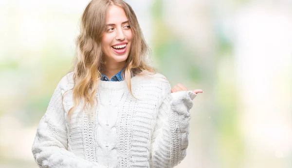 美丽的年轻的金发女子穿着冬季毛衣在孤立的背景微笑与快乐的脸看和指向侧与拇指向上 — 图库照片