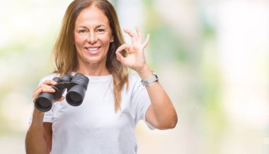 Orta yaş İspanyol kadın parmakları, mükemmel sembolü olan ok işareti yapıyor izole arka plan üzerinde dürbün arıyor