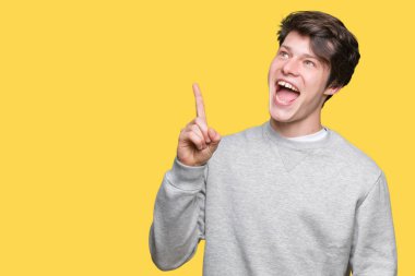 Başarılı fikirle izole arka plan işaret parmağı üzerinde sweatshirt giyen genç yakışıklı sportif adam. Çıktıktan ve mutlu. Bir numara.