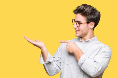 Hayret ve el ile sunulması ve parmak ile işaret ederken kameraya gülümseyen izole arka plan üzerinde gözlük takan genç yakışıklı adam.