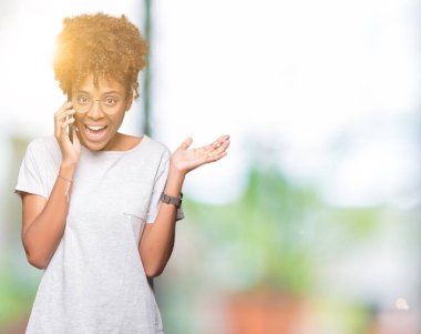 Genç Afro-Amerikan kadın smartphone üzerinde kocaman bir gülümseme ile çığlık zaferini kutluyor ve ellerini kaldırdı izole arka plan çok mutlu ve heyecanlı, kazanan ifade söz
