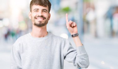 Ve kendinden emin ve mutlu gülümseyerek süre parmak numaralı yukarıyı gösteren izole arka plan üzerinde sweatshirt giyen genç yakışıklı adam.