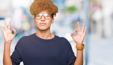 Afro gözlük sakin ol genç yakışıklı adamla ve gülümseyen gözlerle parmak ile meditasyon jest yapıyor kapalı. Yoga kavramı.