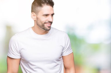 Uzak tarafına yüzünde, doğal ifade gülümseme ile seyir izole arka plan üzerinde rahat beyaz t-shirt giyen genç adam. Kendine güvenen gülüyor.