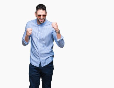 Yakışıklı delikanlı üzerinde güneş gözlüğü takıyor arka plan çok mutlu ve heyecanlı kaldırdı, silah ile kazanan jest yapıyor gülümseyen ve başarı için çığlık izole. Kutlama kavramı.