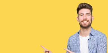 Genç yakışıklı sarışın adam rahat forması giyen gülümseyen ve iki elleri ve parmakları ile tarafına işaret kamera bakıyor.