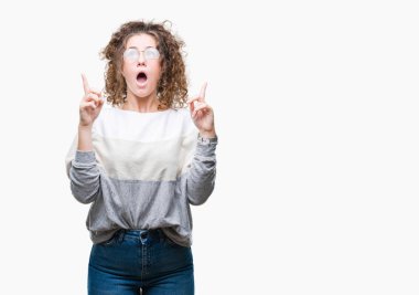 Güzel esmer kıvırcık saçlı Genç kız izole arka plan üzerinde gözlük hayret ve yukarıya bakıp parmakları ile işaret şaşırttı ve silah kaldırdı.