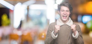 Yakışıklı delikanlı izole arka plan üzerinde kutluyor kış palto giyiyor şaşırttı ve başarı için kaldırdı Kollarını açarak hayret ve gözleri açık. Kazanan kavramı.