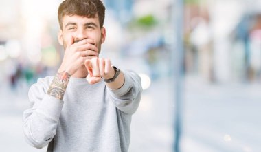 Genç yakışıklı adam giyen kazak izole üzerinde arka plan sizin parmak el kamerasıyla ağzına, utanç ifadesi işaret eden gülme