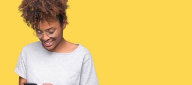 Ayakta ve diş gösterilen kendine güvenen bir gülümsemeyle gülümseyerek mutlu bir yüz ile izole arka plan üzerinde akıllı telefon kullanan genç Afro-Amerikan kadın